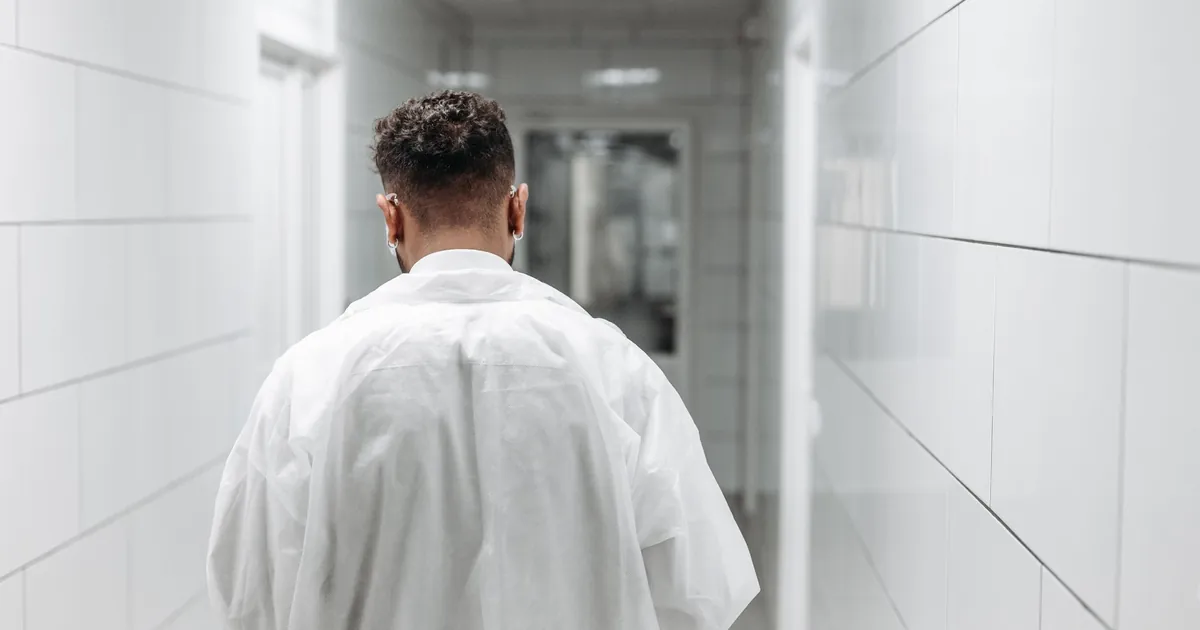A doctor in a white coat walking away down a bright hospital corridor